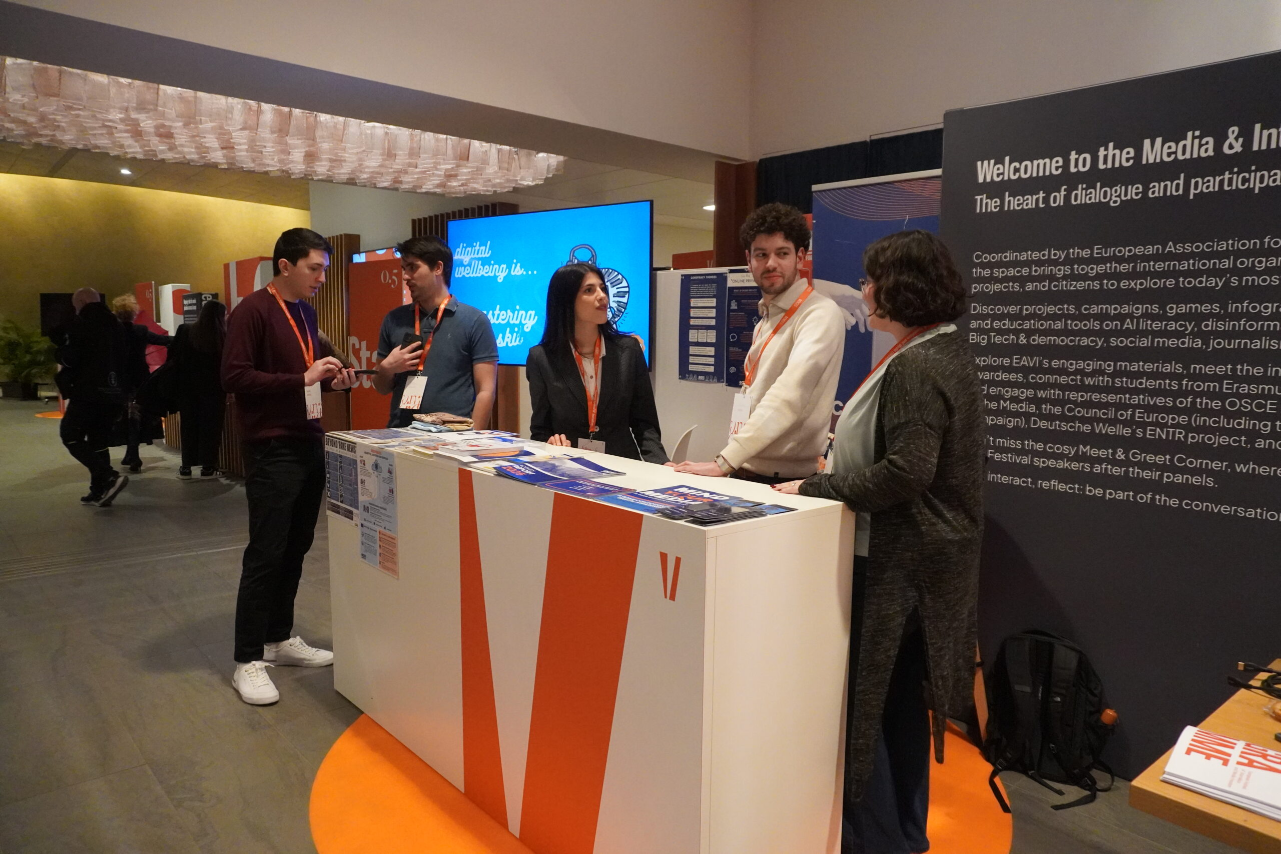 A stand at the Voices Festival exhibition floor with three people standing behind it and other conference participants in the background